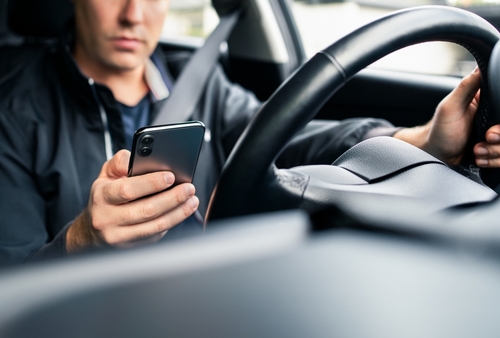 Man using smartphone while driving, highlighting distracted driving risks in rideshare accidents.