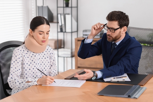Woman with neck brace signing documents while consulting with a rideshare accident lawyer in a professional office setting, emphasizing legal support for Uber and Lyft accident claims.