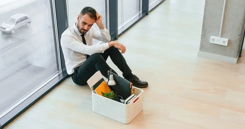 A laid-off employee is sitting on the office floor with his belongings in a box and is contemplating a workers' compensation claim after a sudden termination in Georgia.