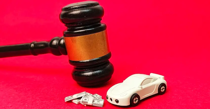 A judge's gavel stands beside a miniature white sports car and stacks of cash against a red background symbolizing a car accident settlement negotiated after a dispute with a health insurance company over injury-related medical expenses in Georgia with help from 1Georgia Personal Injury Lawyers.