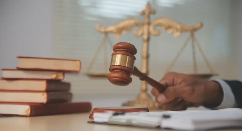 An attorney strikes a gavel on a desk beside a stack of law books and a gold scales of justice in the background, representing the legal process that follows when an insurance dispute arises over whether a policy will cover a car accident claim.