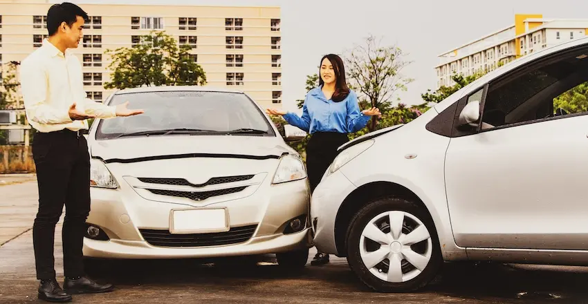 A man and woman stand on either side of two collided vehicles with their hands outstretched in a dispute- illustrating a shared fault scenario where both drivers are arguing over who is responsible and could use help from 1Georgia Personal Injury Lawyers in Georgia.